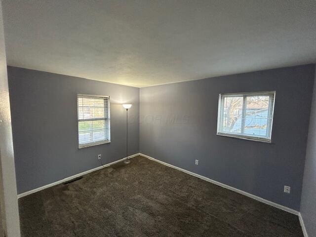 unfurnished room featuring dark carpet, baseboards, and a wealth of natural light