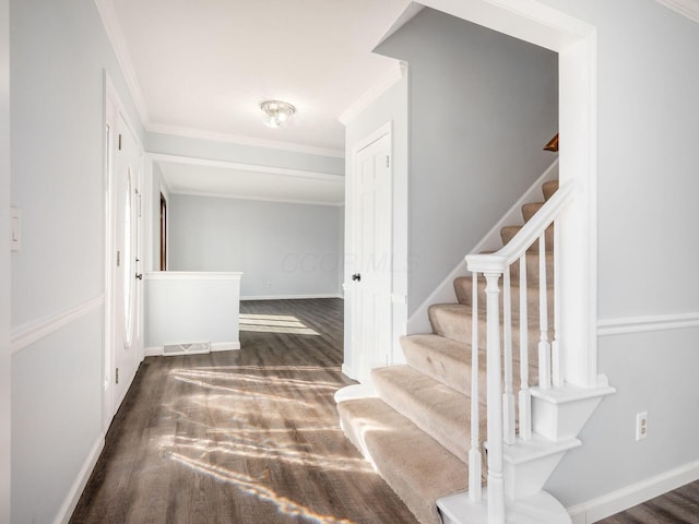 staircase featuring crown molding, wood finished floors, visible vents, and baseboards