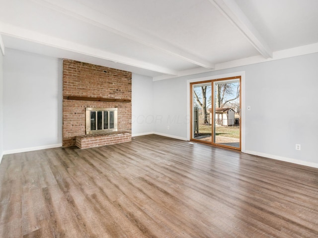 unfurnished living room featuring a brick fireplace, baseboards, beam ceiling, and wood finished floors