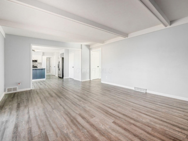 unfurnished living room with visible vents, beamed ceiling, baseboards, and wood finished floors