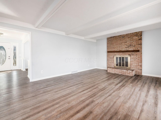 unfurnished living room featuring a brick fireplace, baseboards, beam ceiling, and wood finished floors