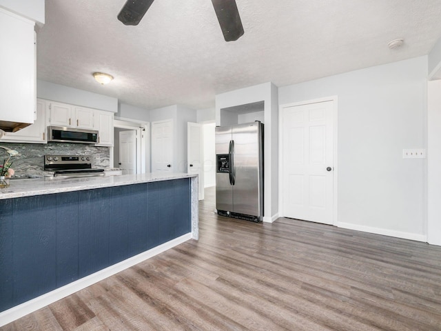 kitchen featuring decorative backsplash, appliances with stainless steel finishes, white cabinets, wood finished floors, and a peninsula