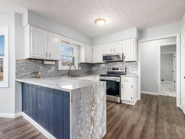 kitchen with stainless steel appliances, white cabinetry, a sink, and light stone counters