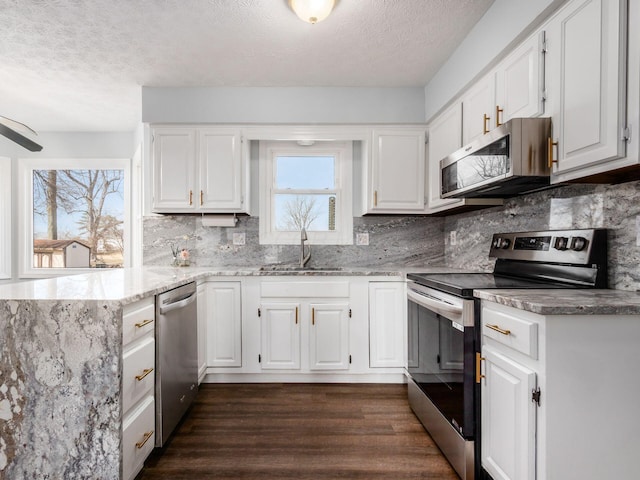 kitchen featuring light stone counters, stainless steel appliances, dark wood-type flooring, a sink, and white cabinetry