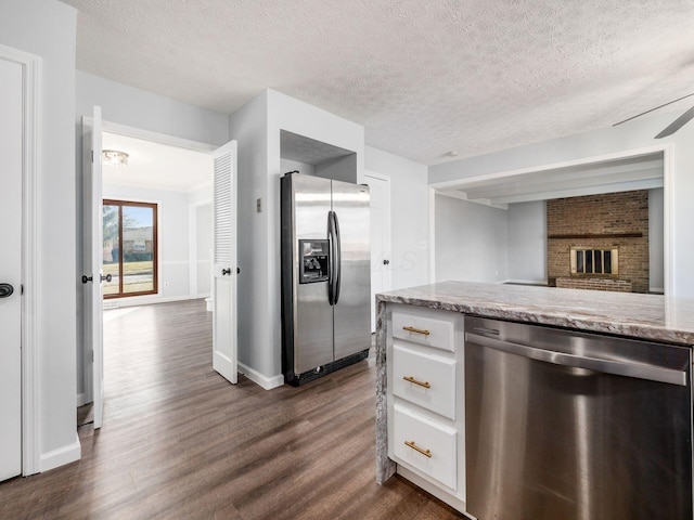 kitchen featuring a textured ceiling, stainless steel appliances, dark wood-style flooring, white cabinetry, and light stone countertops