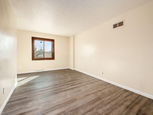 unfurnished room featuring dark wood finished floors, visible vents, and baseboards