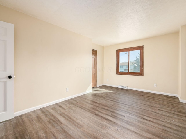 unfurnished room featuring visible vents, a textured ceiling, baseboards, and wood finished floors