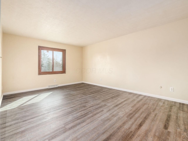 spare room featuring baseboards, visible vents, and wood finished floors