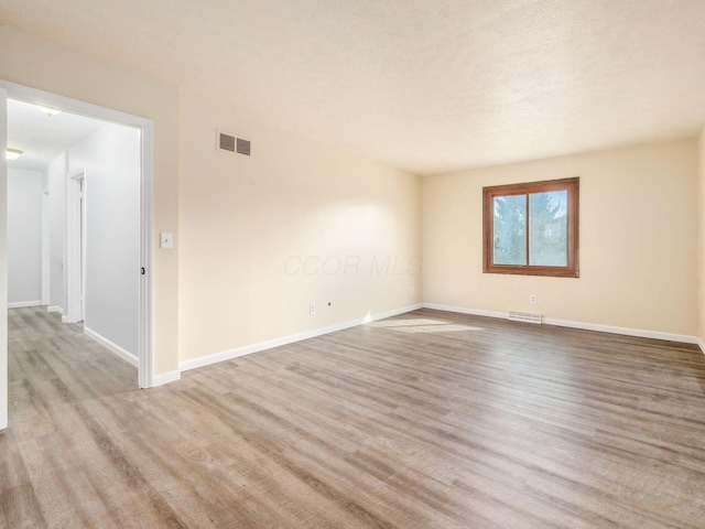 empty room featuring baseboards, visible vents, and wood finished floors