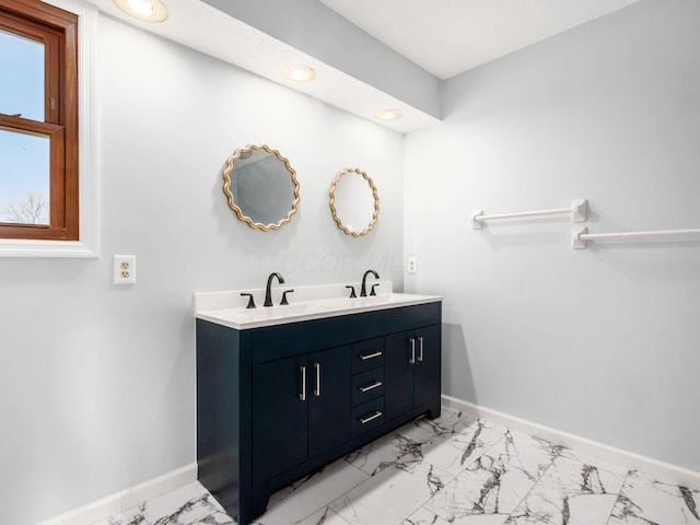 full bath featuring double vanity, marble finish floor, baseboards, and a sink