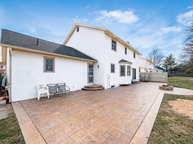 rear view of property featuring roof with shingles, fence, a patio, and stucco siding