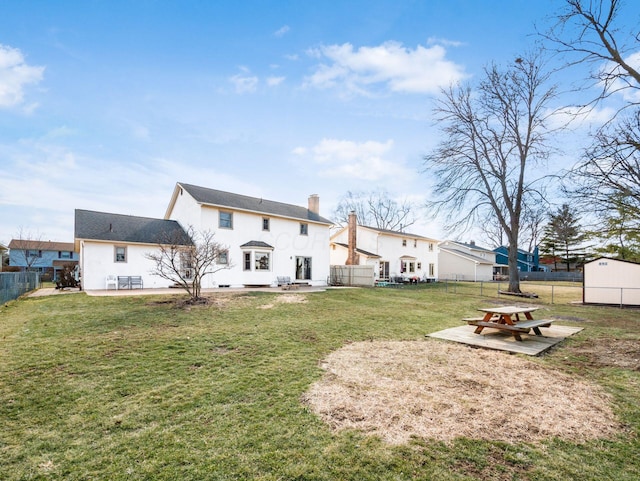 back of house featuring a yard, a fenced backyard, a chimney, and a patio