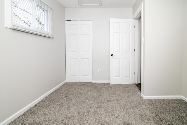 unfurnished bedroom featuring carpet floors, a closet, attic access, and baseboards