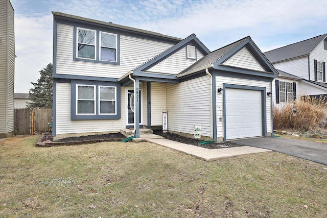 traditional-style home with an attached garage, a front lawn, fence, and aphalt driveway