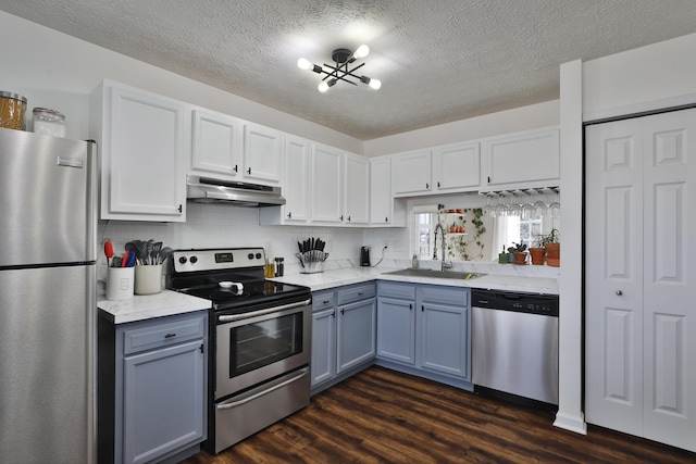 kitchen with appliances with stainless steel finishes, dark wood-type flooring, under cabinet range hood, white cabinetry, and a sink