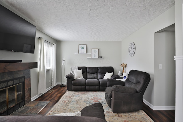 living area with baseboards, a textured ceiling, a tiled fireplace, and wood finished floors