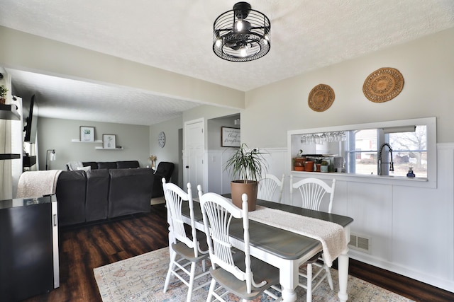 dining space featuring visible vents, dark wood-style flooring, a textured ceiling, and wainscoting