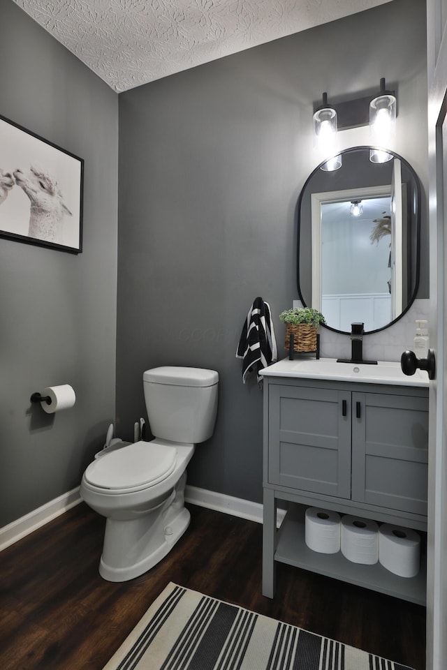 half bath with a textured ceiling, toilet, wood finished floors, vanity, and baseboards