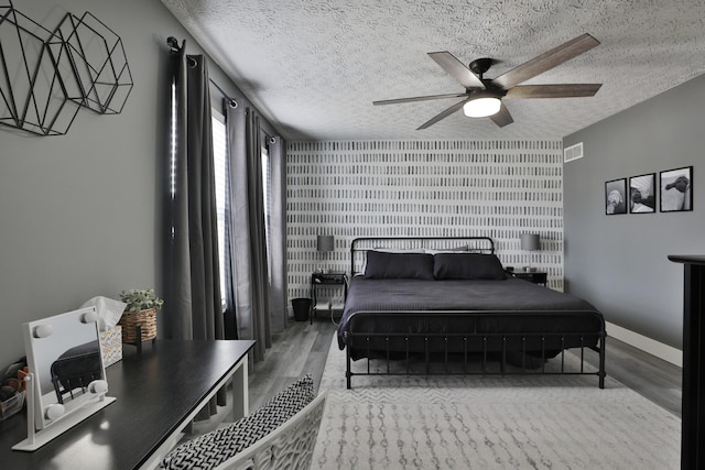 bedroom with ceiling fan, a textured ceiling, baseboards, and wood finished floors