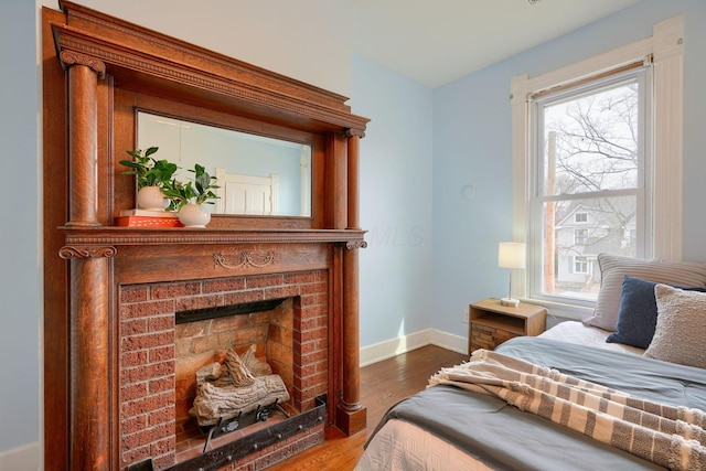 bedroom with a brick fireplace, baseboards, and wood finished floors