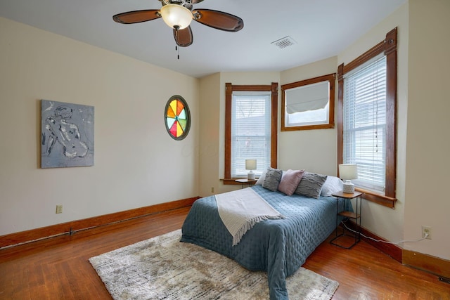 bedroom with multiple windows, wood finished floors, visible vents, and baseboards