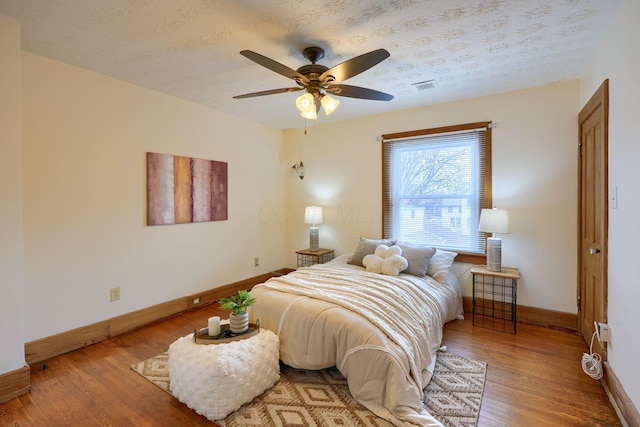 bedroom with visible vents, a textured ceiling, baseboards, and wood finished floors