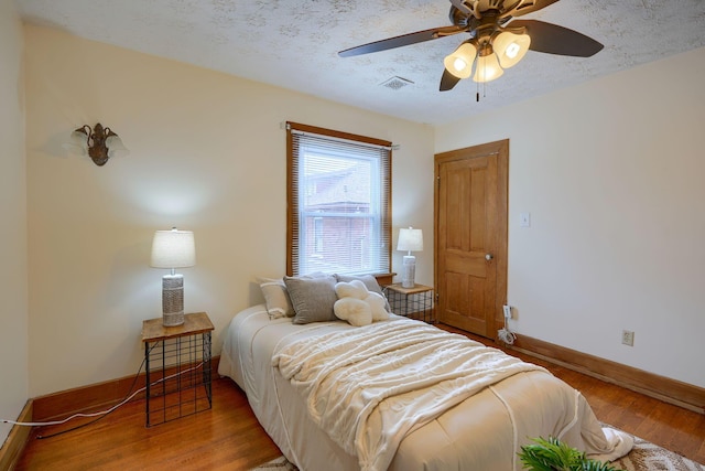 bedroom featuring a textured ceiling, wood finished floors, a ceiling fan, visible vents, and baseboards