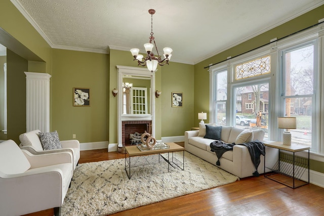 living area featuring a fireplace, wood finished floors, baseboards, an inviting chandelier, and crown molding