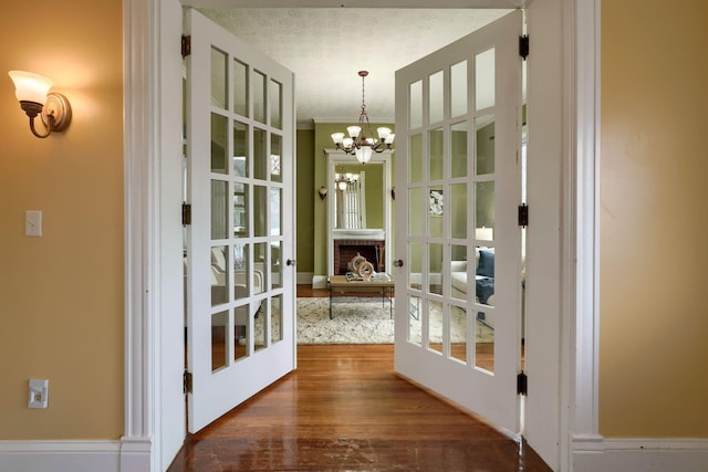 doorway with a textured ceiling, dark wood finished floors, a notable chandelier, and french doors