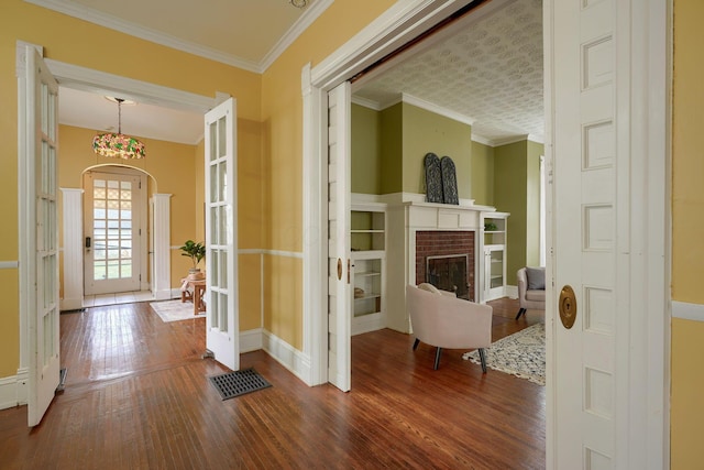 foyer featuring dark wood-style floors, ornamental molding, a brick fireplace, and baseboards