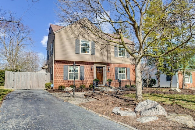 colonial house with a gate, brick siding, and fence