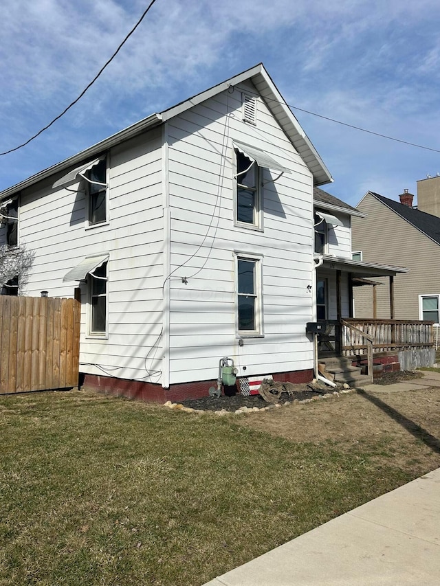 rear view of property featuring covered porch, fence, and a lawn