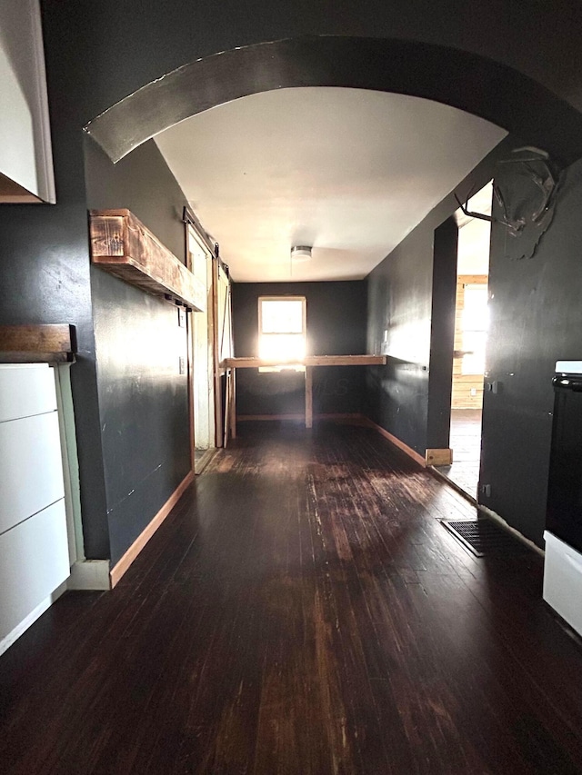 hall featuring arched walkways, wood-type flooring, and baseboards