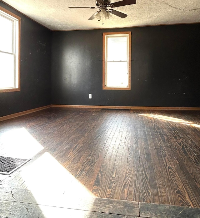 empty room featuring a textured ceiling, hardwood / wood-style floors, and baseboards