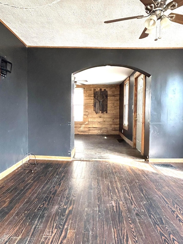 unfurnished room with arched walkways, a ceiling fan, wooden walls, a textured ceiling, and wood finished floors