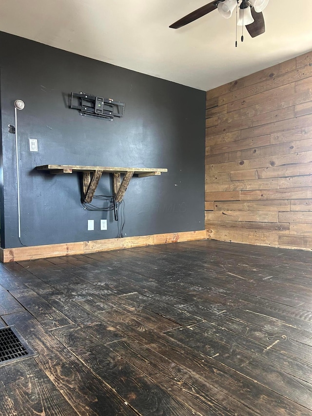 unfurnished room featuring visible vents, wooden walls, a ceiling fan, and wood finished floors