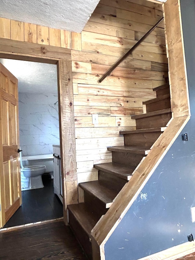 stairs featuring a textured ceiling, wood walls, and wood-type flooring