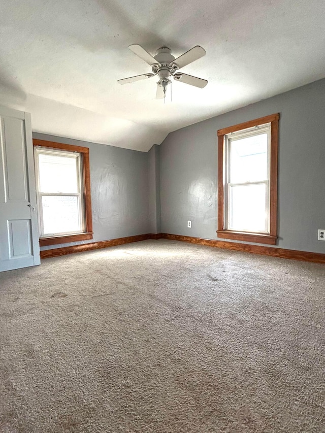 empty room featuring a wealth of natural light, baseboards, vaulted ceiling, and carpet flooring