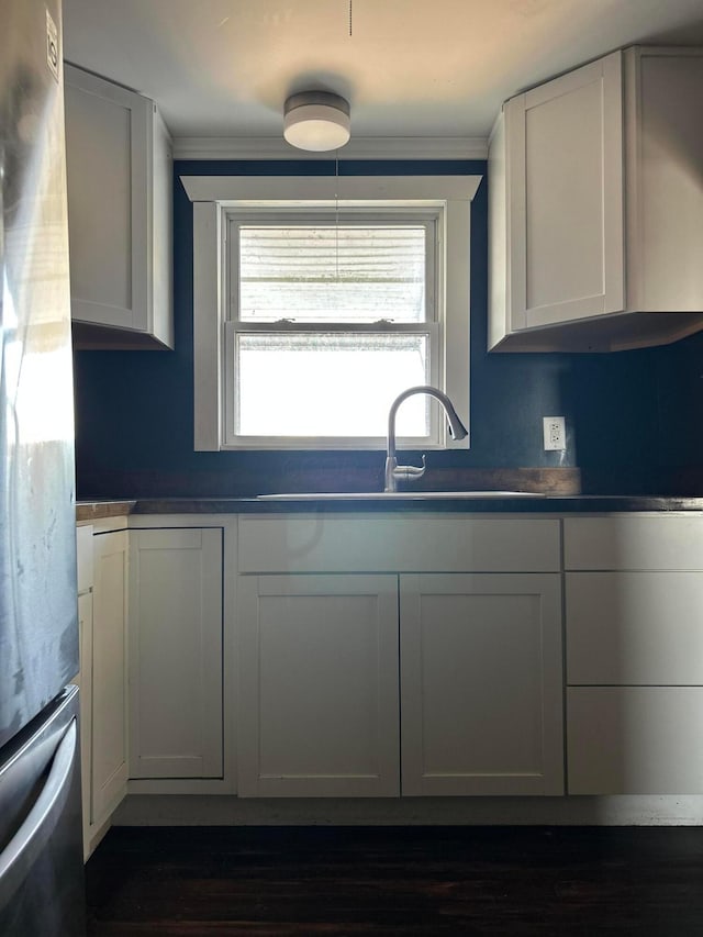 kitchen featuring freestanding refrigerator, a sink, dark countertops, and white cabinetry