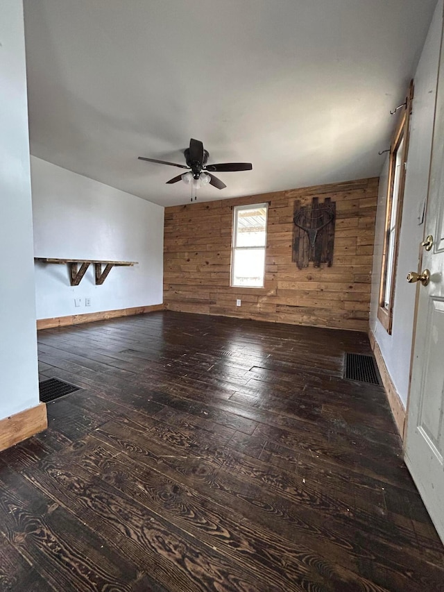 unfurnished living room featuring visible vents, wooden walls, a ceiling fan, and wood-type flooring