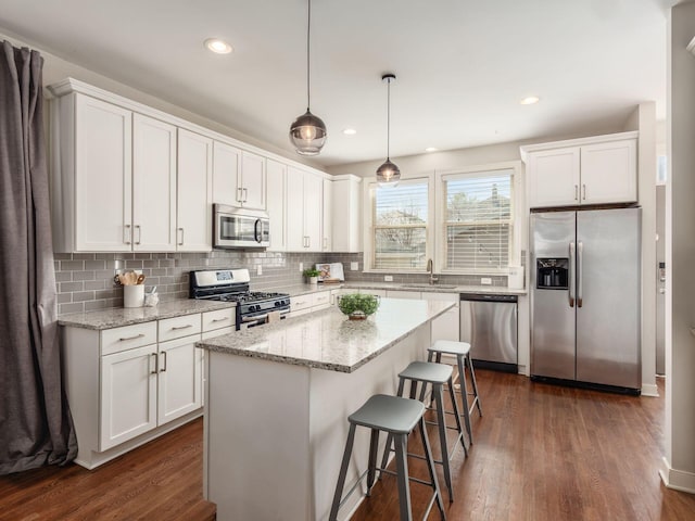 kitchen featuring dark wood finished floors, stainless steel appliances, a kitchen bar, white cabinetry, and backsplash