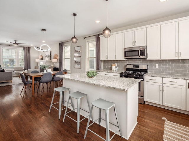 kitchen featuring stainless steel appliances, open floor plan, dark wood finished floors, and tasteful backsplash