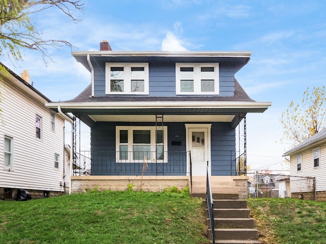 view of front of property with covered porch, a chimney, a front lawn, and roof with shingles