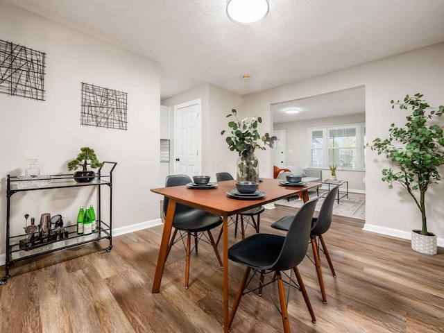 dining area featuring a textured ceiling, baseboards, and wood finished floors