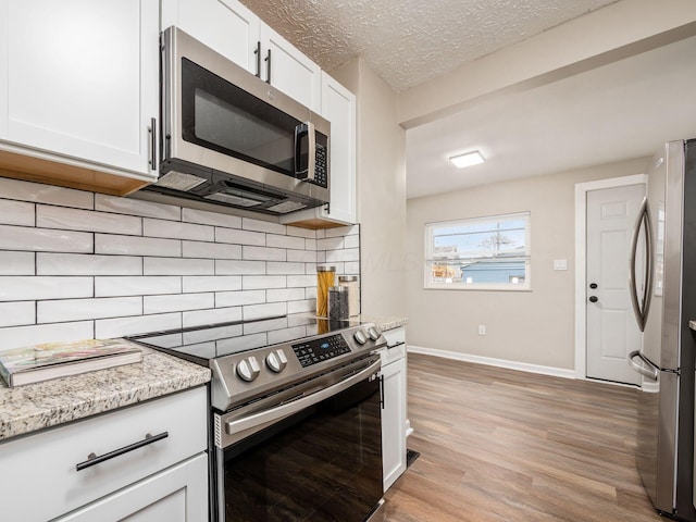 kitchen featuring light wood finished floors, white cabinets, stainless steel appliances, a textured ceiling, and backsplash