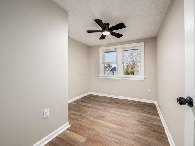 spare room featuring a textured ceiling, wood finished floors, a ceiling fan, and baseboards