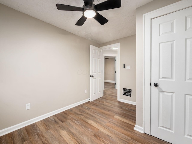 interior space featuring a textured ceiling, ceiling fan, wood finished floors, visible vents, and baseboards