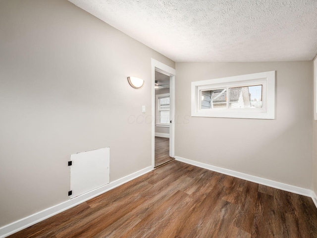 empty room with lofted ceiling, a textured ceiling, baseboards, and wood finished floors