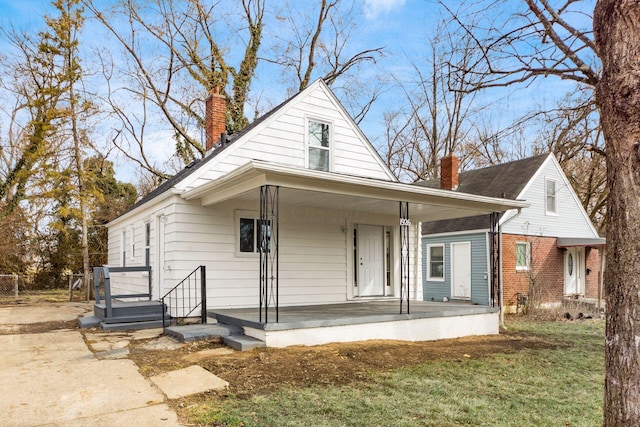 view of front of property featuring a front yard, covered porch, a chimney, and brick siding