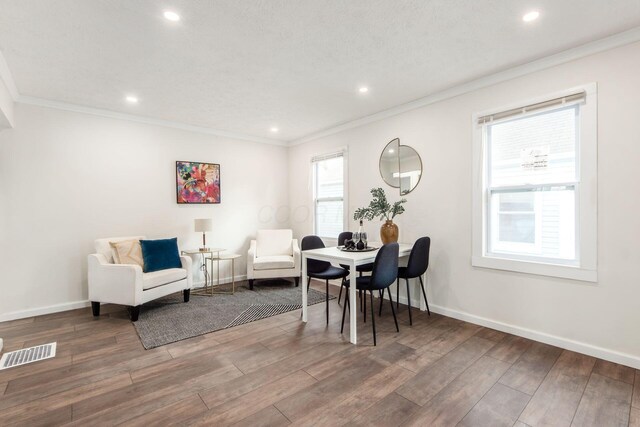 living area with baseboards, wood finished floors, visible vents, and crown molding